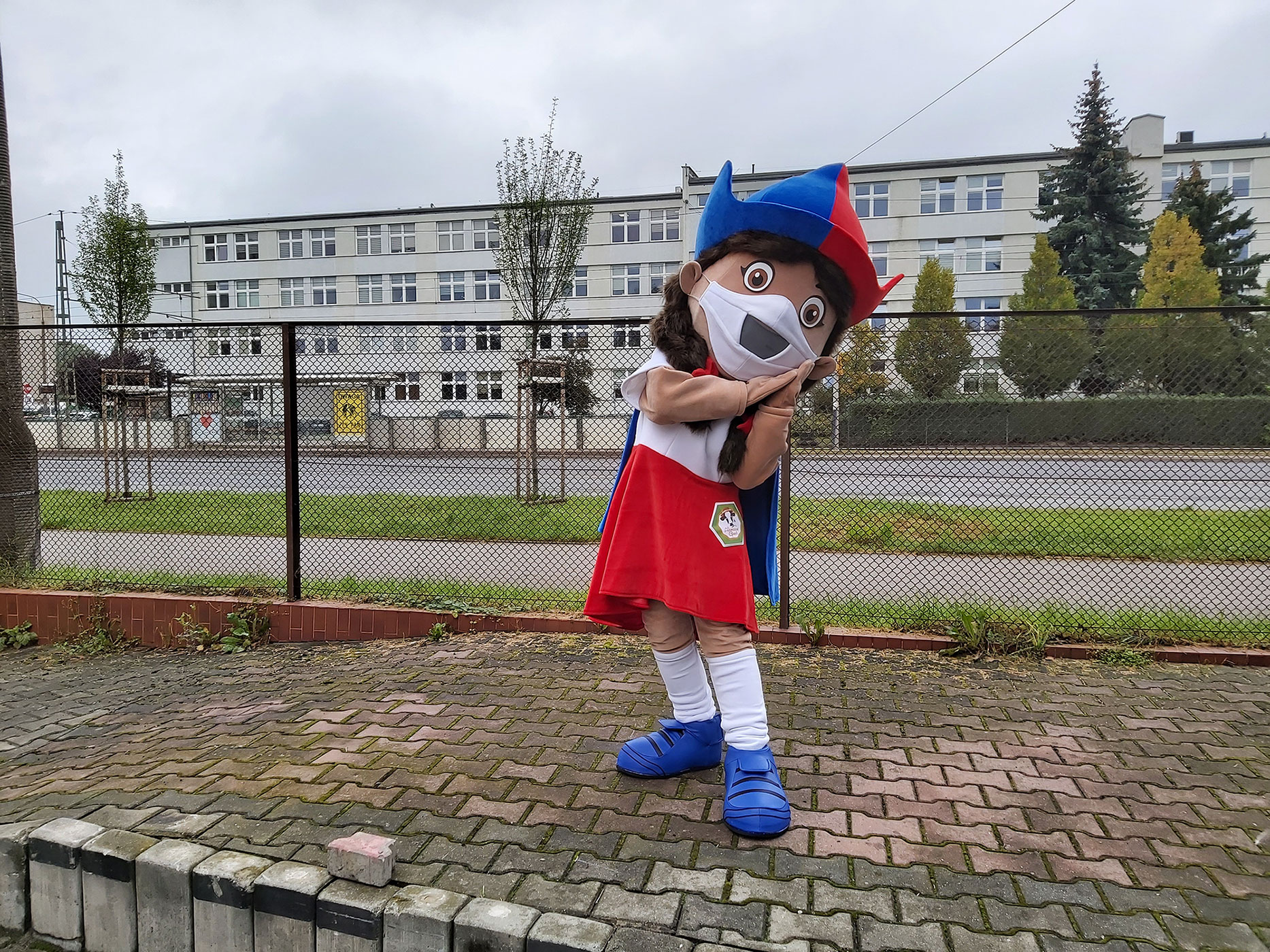 Na fotografii widnieje strój reklamowy dziewczyna stojący na jednej z krakowskich ulic. W tle chodnik, jezdnia i budynek biurowy